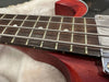 Close-up of vintage electric bass guitar fretboard with metal strings and red wooden body on beige fabric background