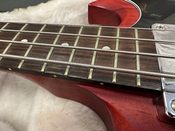 Close-up of vintage electric bass guitar fretboard with metal strings and red wooden body on beige fabric background