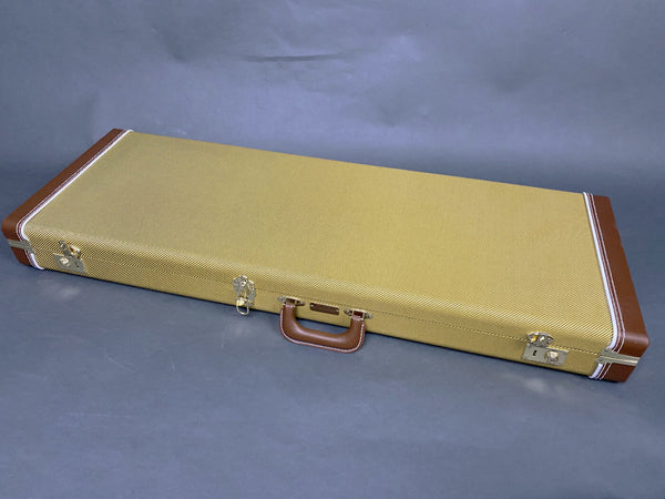 Closed tweed and brown leather guitar case with metal latches and handle on gray background