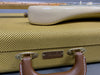Close-up of vintage Fender guitar case with tweed fabric texture and brown leather handle, showing the bottom part of a white Fender electric guitar resting on top.