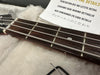 Close-up of bass guitar fretboard with metal strings, tuning peg, and a note highlighting attention to detail in multiple languages on soft fabric background, including Allen wrench tool for guitar setup.