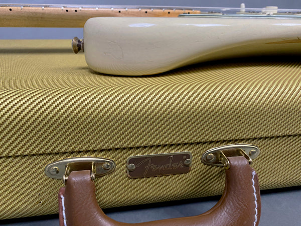 Close-up of vintage Fender guitar case with tweed fabric texture and brown leather handle, showing the bottom part of a white Fender electric guitar resting on top.