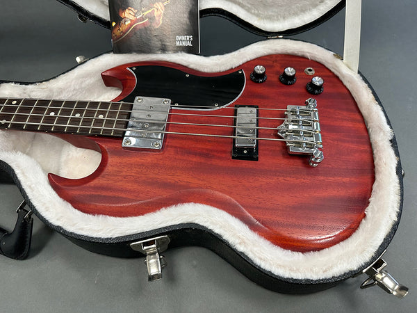 Cherry red electric bass guitar with black pickguard and chrome hardware in a white fur-lined hard case with owner's manual