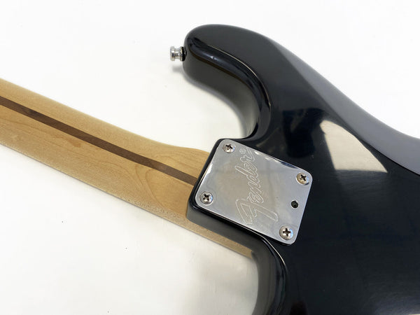 Close-up of Fender electric guitar neck joint with maple neck, walnut stripe, and black body showing engraved Fender neck plate and strap button