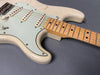 Close-up of vintage white electric guitar body and maple neck showing scratches and wear on the finish and a light blue pickguard with three single coil pickups and volume control knob