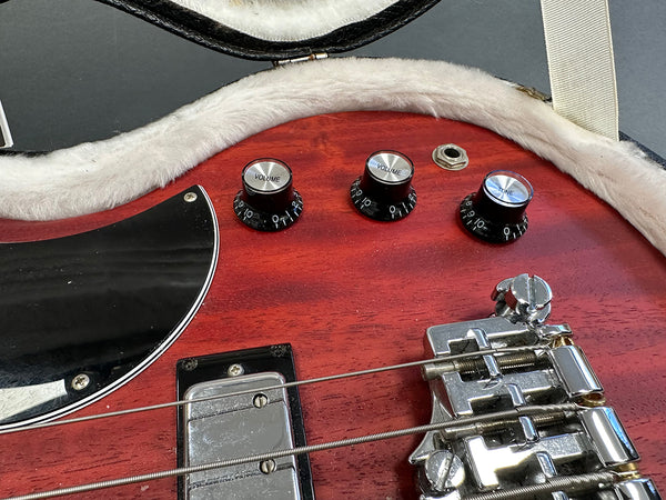 Close-up of red electric guitar body showing volume and tone control knobs, strings, and chrome bridge hardware in plush-lined guitar case