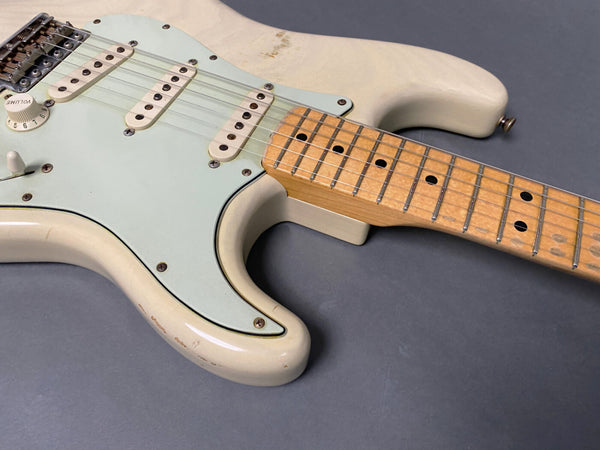 Close-up of vintage white electric guitar body and maple neck showing scratches and wear on the finish and a light blue pickguard with three single coil pickups and volume control knob