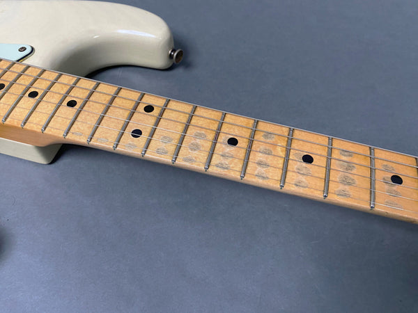 Close-up of maple guitar neck with visible wear and dot inlays on light-colored electric guitar body against gray background