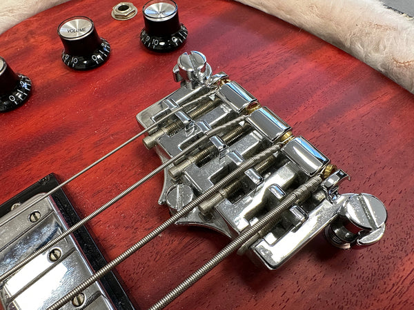 Close-up of electric guitar bridge and strings on red wood body with volume and tone control knobs visible