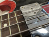 Close-up of electric bass guitar fretboard and chrome pickup with metal strings and red body edge visible