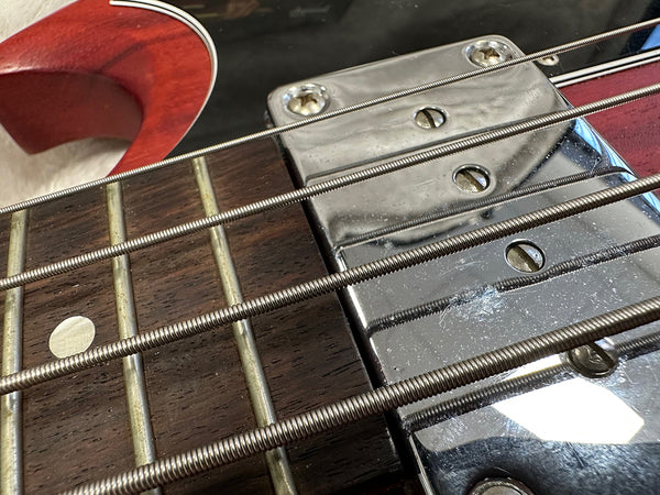 Close-up of electric bass guitar fretboard and chrome pickup with metal strings and red body edge visible