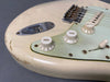 Close-up of vintage white electric guitar body showing volume and tone control knobs, input jack, and worn paint finish with scratches and chips