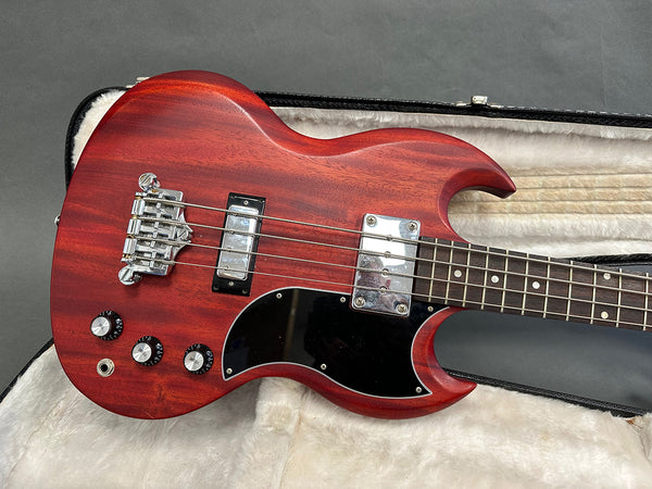 Vintage red electric bass guitar with dual humbucker pickups and black pickguard resting in plush-lined guitar case