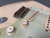 Close-up of vintage electric guitar bridge, tone and volume control knobs, and single-coil pickups on worn cream finish body