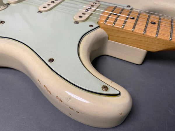 Close-up of vintage cream electric guitar body with worn finish and light green pickguard showing screw details and maple fretboard