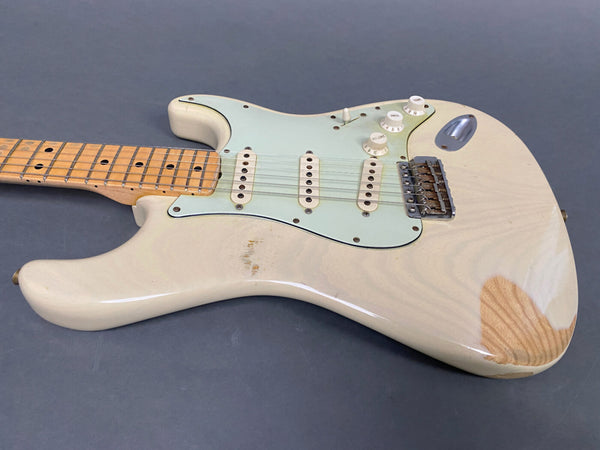 Vintage white electric guitar with maple neck and three single-coil pickups on gray background