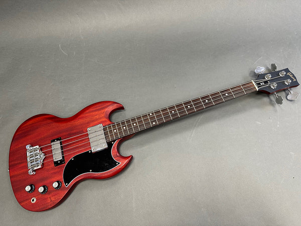 Gibson SG style electric bass guitar with cherry red finish, black pickguard, and chrome hardware on grey background