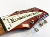 Close-up of vintage Rickenbacker guitar headstock with six tuning pegs and white logo plate, made in U.S.A., on a reddish wooden finish.