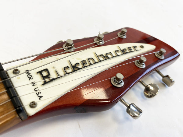 Close-up of vintage Rickenbacker guitar headstock with six tuning pegs and white logo plate, made in U.S.A., on a reddish wooden finish.