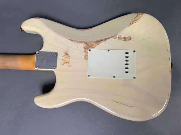 Back view of vintage white electric guitar with worn and chipped finish, metal neck plate with Fender logo, on gray background