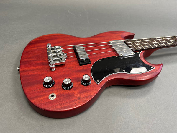 Red electric bass guitar with black pickguard and chrome hardware on gray background