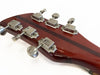 Close-up of vintage guitar headstock with six metal tuning pegs and dark wood stripe on red-brown finish background