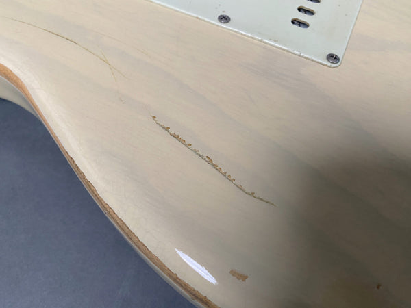 Close-up of vintage white electric guitar body showing worn and chipped finish damage near the edge and backplate screws.