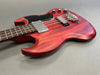 Electric bass guitar with red wooden finish and black pickguard on gray background