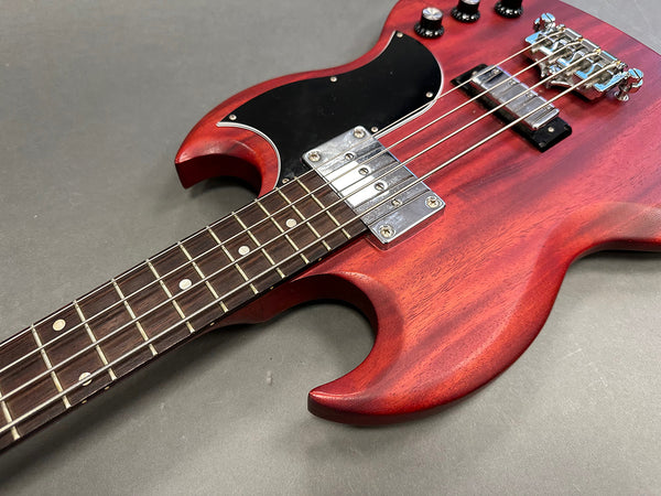 Close-up of red electric bass guitar body and fretboard with chrome pickups and black pickguard on gray background