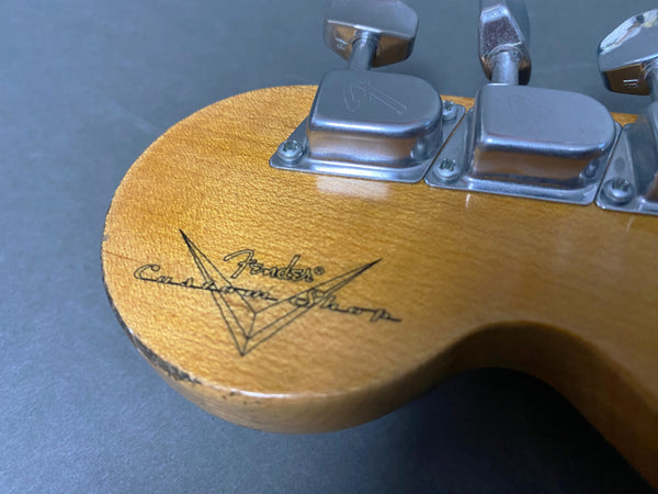 Close-up of the back of a Fender Custom Shop guitar headstock with tuning pegs and visible Fender Custom Shop logo on natural wood finish.