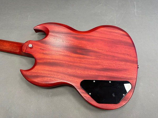 Back of red mahogany electric guitar body with black control cavity cover on gray background