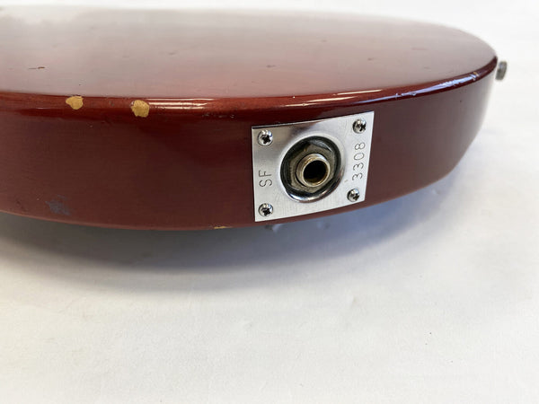 Close-up of red electric guitar output jack plate with visible wear and scratches on body edge