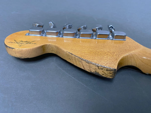 Close-up of vintage Fender Custom Shop guitar headstock with aged wood and chrome tuning pegs on a dark surface