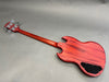 Back view of red electric bass guitar with natural wood grain finish and chrome tuning pegs on gray background