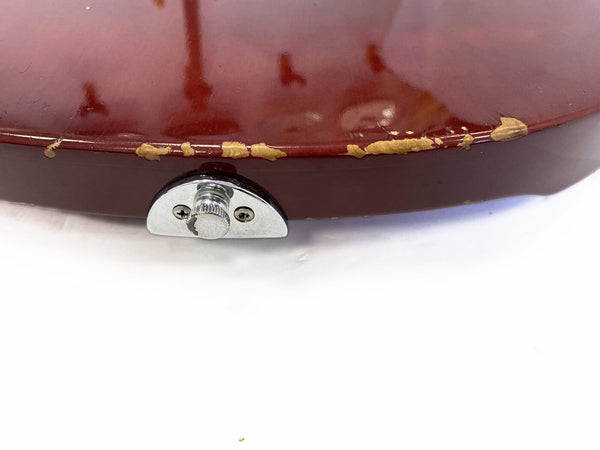 Close-up of worn red guitar body edge with paint chipping and metal strap button installed on white background