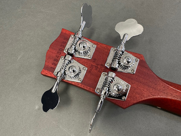 Close-up of bass guitar headstock showing chrome Grover tuning machines on mahogany wood with serial number and "Made in USA" stamp