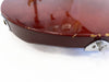 Close-up of worn dark red electric guitar body edge showing paint chips and metal strap button on white background