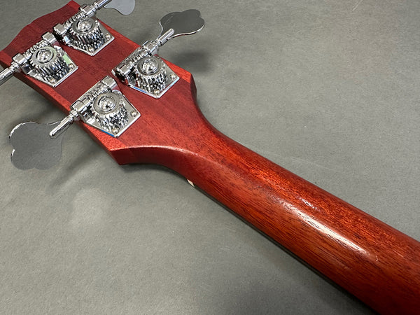 Close-up of bass guitar headstock back showing chrome tuning pegs and reddish-brown wooden neck