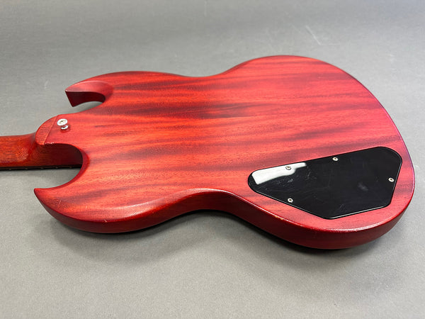 Back view of red electric guitar body with black plastic cover plate on grey surface