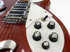 Close-up of red electric guitar featuring white pickguard, five black control knobs labeled Bass Tone, Bass Volume, Treble Tone, Treble Volume, and a toggle switch, showcasing vintage hardware and strings