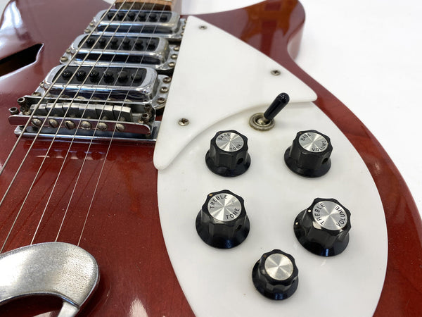 Close-up of red electric guitar featuring white pickguard, five black control knobs labeled Bass Tone, Bass Volume, Treble Tone, Treble Volume, and a toggle switch, showcasing vintage hardware and strings