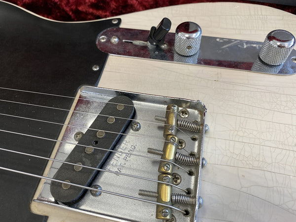 Close-up of vintage Fender guitar bridge and pickup with chrome control knobs on white cracked finish guitar body