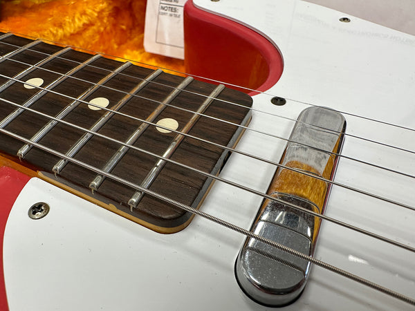 Close-up of electric guitar bridge, strings, and rosewood fretboard with dot inlays on white pickguard and red sunburst body finish
