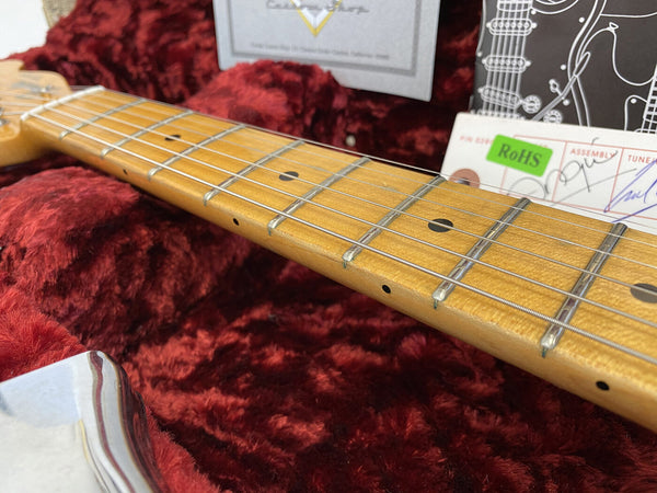 Close-up of maple guitar neck and fretboard with metal frets and dot inlays, resting in red plush guitar case interior with warranty and certification cards in background