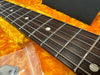 Close-up of guitar fretboard with metal frets and dot inlays on dark wood, resting on orange plush guitar case lining with plastic bag containing guitar accessory