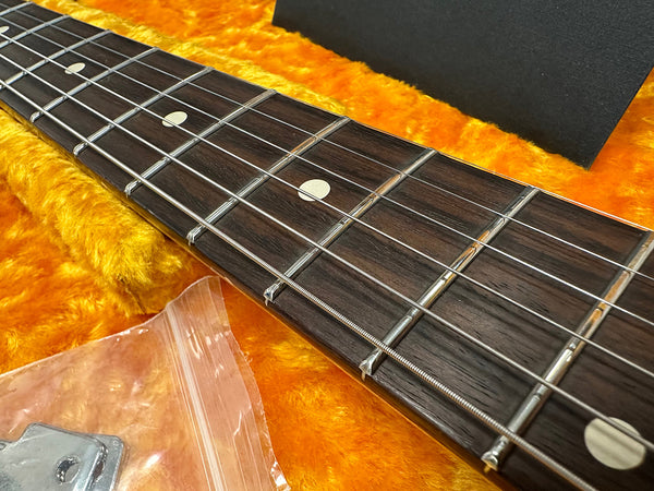 Close-up of guitar fretboard with metal frets and dot inlays on dark wood, resting on orange plush guitar case lining with plastic bag containing guitar accessory