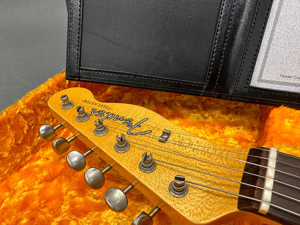 Close-up of Fender Telecaster guitar headstock with tuning pegs inside an orange plush-lined guitar case