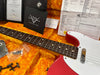 Close-up of red and white Fender electric guitar neck and body with rosewood fretboard, set in a bright orange plush case, showing Fender Custom Care card, warranty certificate, and hardware parts.