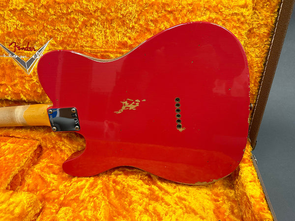 Back of red Fender electric guitar with visible wear and chip marks resting in orange plush-lined Fender guitar case