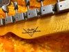 Close-up of vintage Fender Custom Shop guitar headstock with metal tuning pegs and natural wood finish on a bright yellow textured background